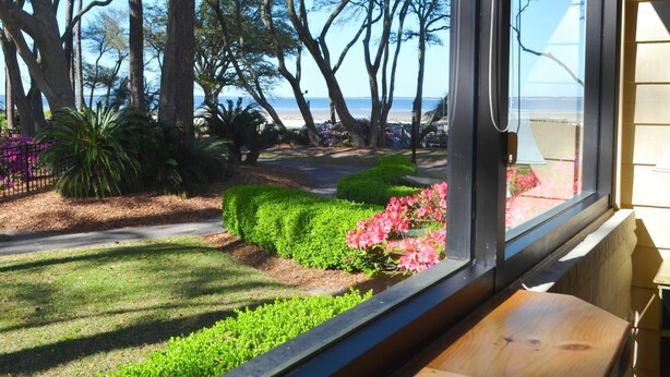 Une vue depuis une fenêtre donnant sur un jardin aménagé, avec un sentier, des arbres et, au loin, une plage.