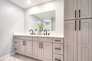 Un baño con lavamanos doble, un espejo grande y gabinetes grises.