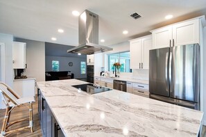 A modern kitchen with white cabinets, a stainless steel refrigerator, and a marble countertop.