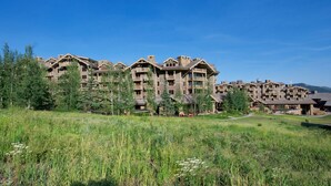 A large resort with multiple buildings featuring a rustic architectural style, surrounded by lush greenery and a clear sky. - 6/20 to 6/27 or 11/22 to 11/29, Four Seasons 3 BDRM, 3 Full Bath, Jackson Hole (Teton Village)