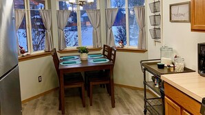 Una cocina con una mesa de comedor, armarios de madera, un refrigerador y una ventana con cortinas.