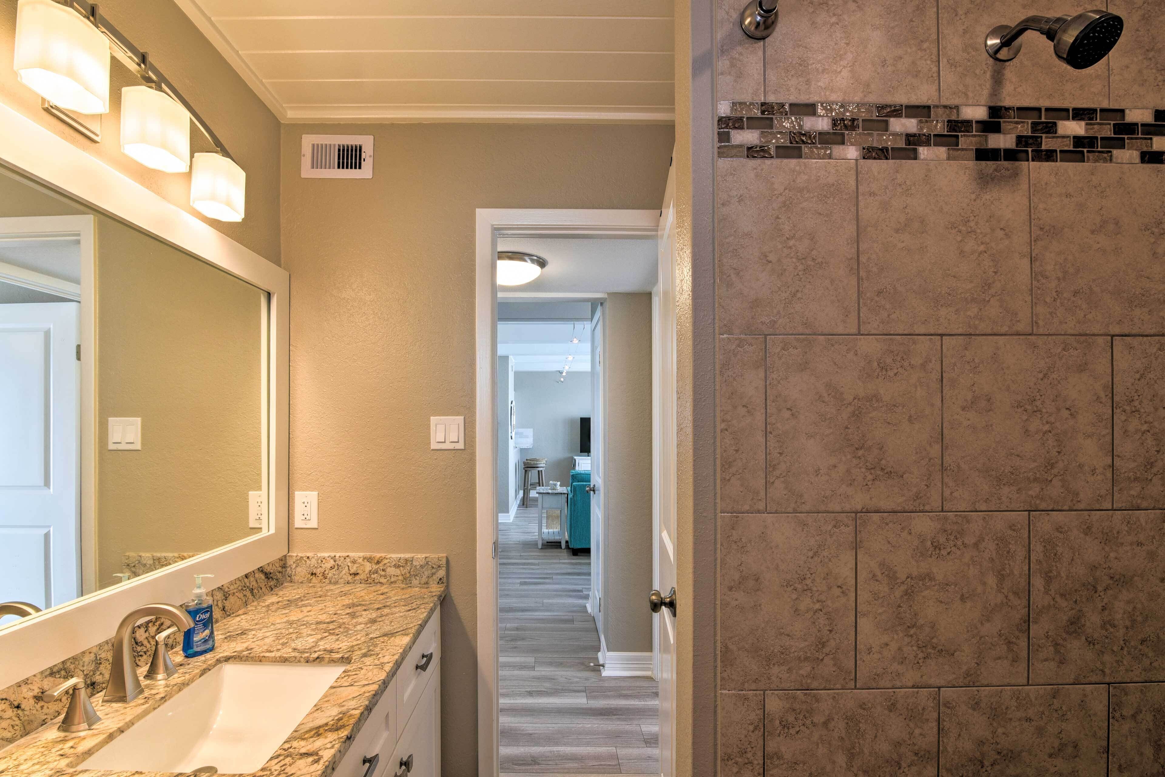 A bathroom with a sink, mirror, and shower area.