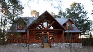 A log cabin with a stone foundation, large windows, and a porch.