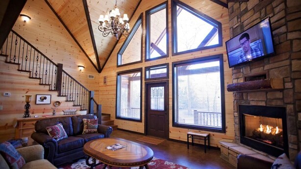 A cozy log cabin interior with a fireplace, a television mounted on the wall, and a staircase leading to an upper level.