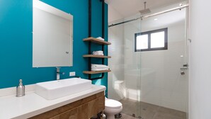 Ein modernes Badezimmer mit Waschbecken in Weiß, Holzwaschtisch, einer Duschkabine aus Glas und teal-farbenen Wänden.