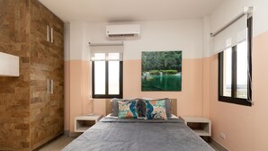 Ein Schlafzimmer mit Bett, Nachttischen, einem Kleiderschrank, einem Fenster und einer Wand-Klimaanlage.