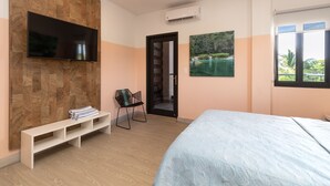 Ein Schlafzimmer mit einem Bett, einem an einer Holzwand montierten Fernseher, einer Bank mit Büchern, einem Sessel und einem Landschaftsbild.