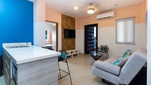 Eine moderne Küche mit weißer Arbeitsplatte und integriertem Herd. Es gibt eine Sitzecke mit einem grauen Sofa und einem kleinen Tisch.