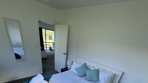 A modern hotel room with a large bed, a bedside table, a mirror, and a view of the outdoor area. - Coopers Haven Beachfront House (Coopers Beach)