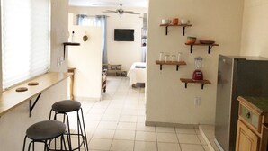 A kitchen with a refrigerator, bar stools, and shelves with kitchenware. - Cozy & Lovely Studio! w/ DISNEY+, NETFLIX & More!! (zamora)
