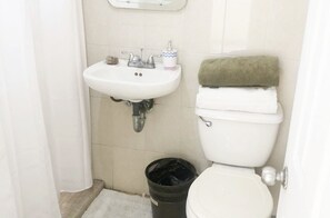 Un baño pequeño con un lavamanos blanco, un inodoro y un cubo de basura negro.