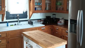 Een keuken met houten kastjes, een roestvrijstalen koelkast, een inbouwoven en een raam met gordijn.