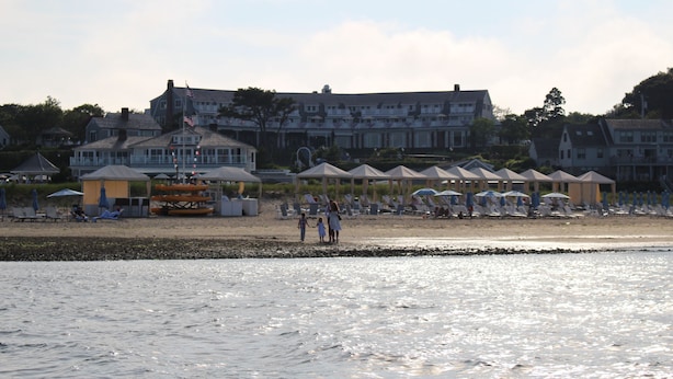 Ett hotell vid stranden med flera parasoller, solstolar och en stor byggnad i bakgrunden.