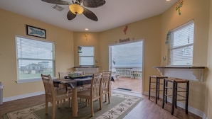 A dining area with a table and chairs, a ceiling fan, and a view of the beach through the windows. - Stunning beach views-100 steps to beach-Huge deck (Surfside Beach)
