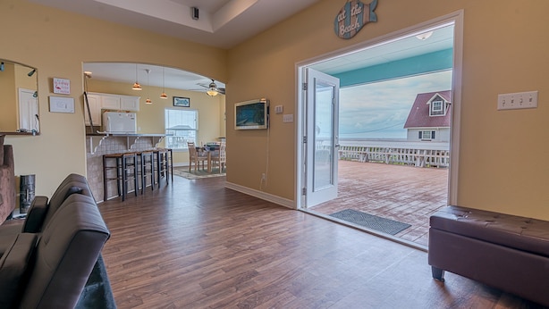A spacious living area with a wooden floor, a large sliding glass door leading to a balcony, and a kitchen in the background. - Stunning beach views-100 steps to beach-Huge deck (Surfside Beach)