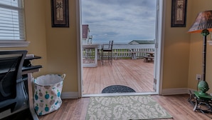 A room with a wooden deck, a sliding glass door leading to the deck, a chair, a small table, a lamp, and a trash can. - Stunning beach views-100 steps to beach-Huge deck (Surfside Beach)