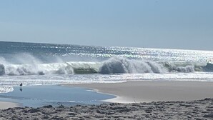 Una playa con olas rompiendo en la orilla, un cielo despejado y una persona de pie en el agua.
