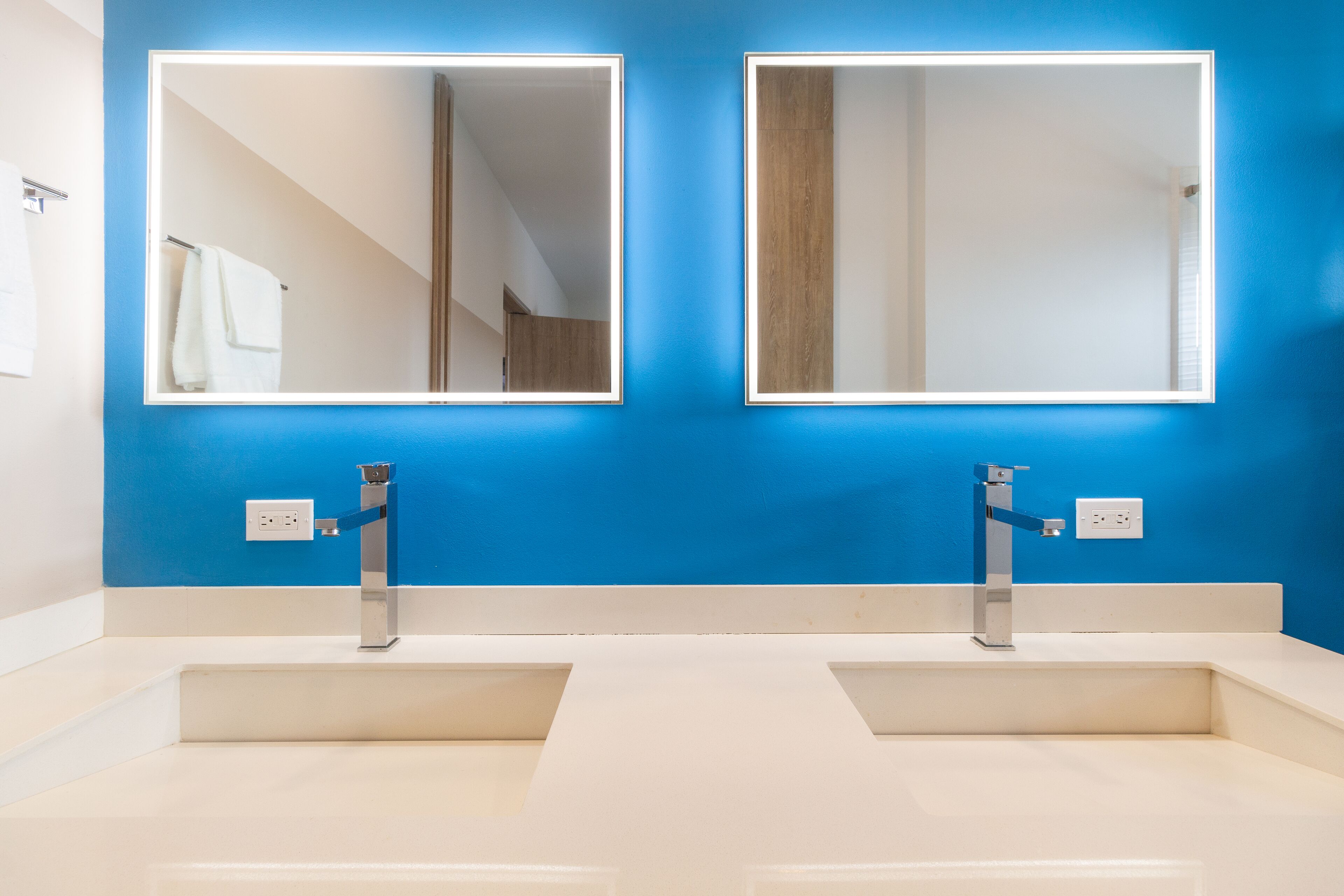 Ein Badezimmer mit zwei Waschbecken, jeweils mit einem Spiegel darüber. Die Wände sind blau gestrichen, und ein Handtuch hängt auf einem Haken.