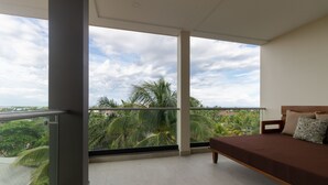 A balcony with a bed, large windows, and a view of palm trees.