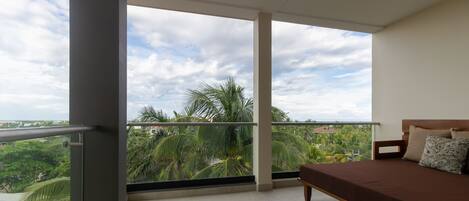 Un balcón con cama, ventanas amplias y vista a palmeras.