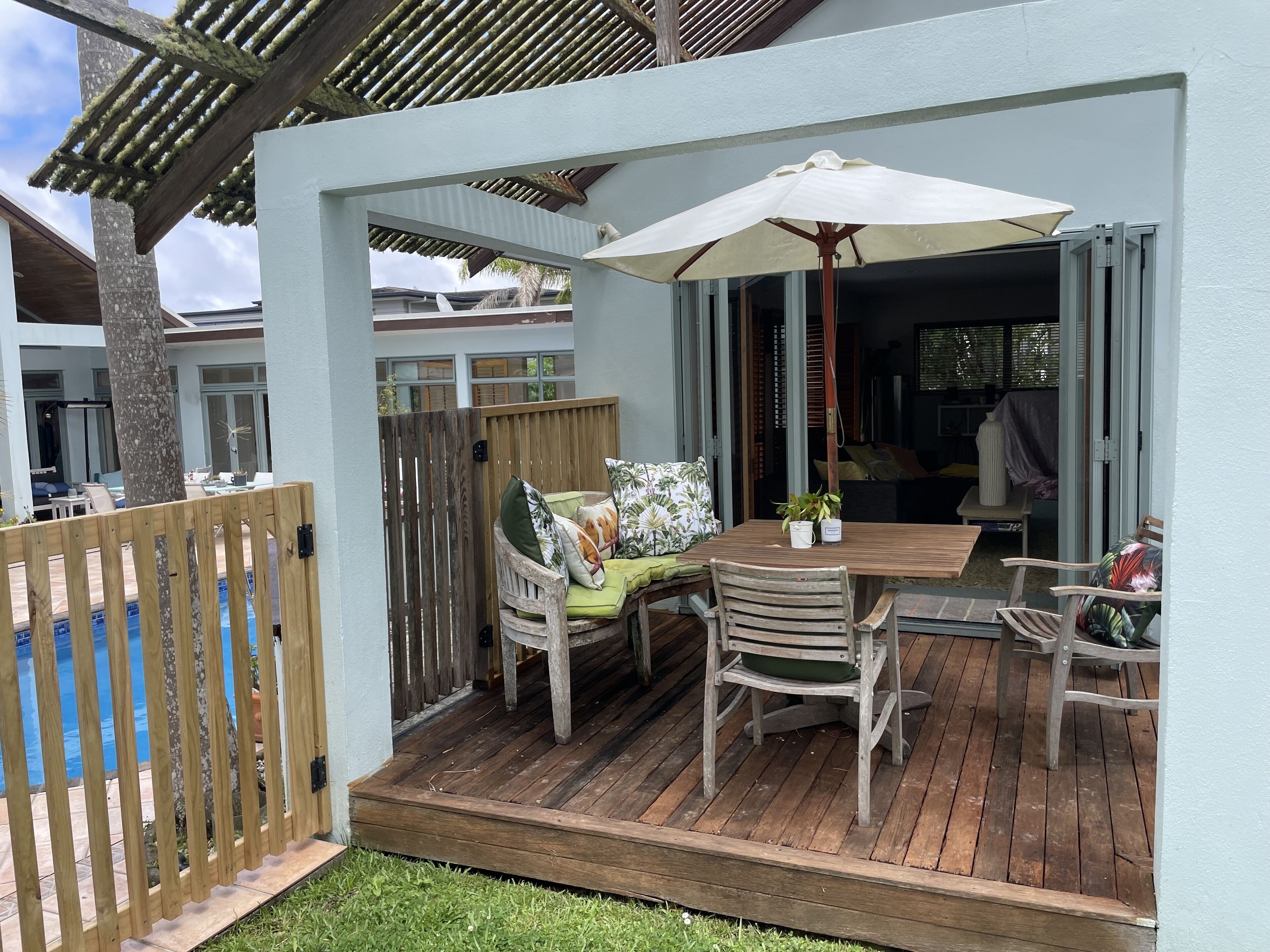 A wooden deck with a table and chairs, a white umbrella, and a wooden fence.