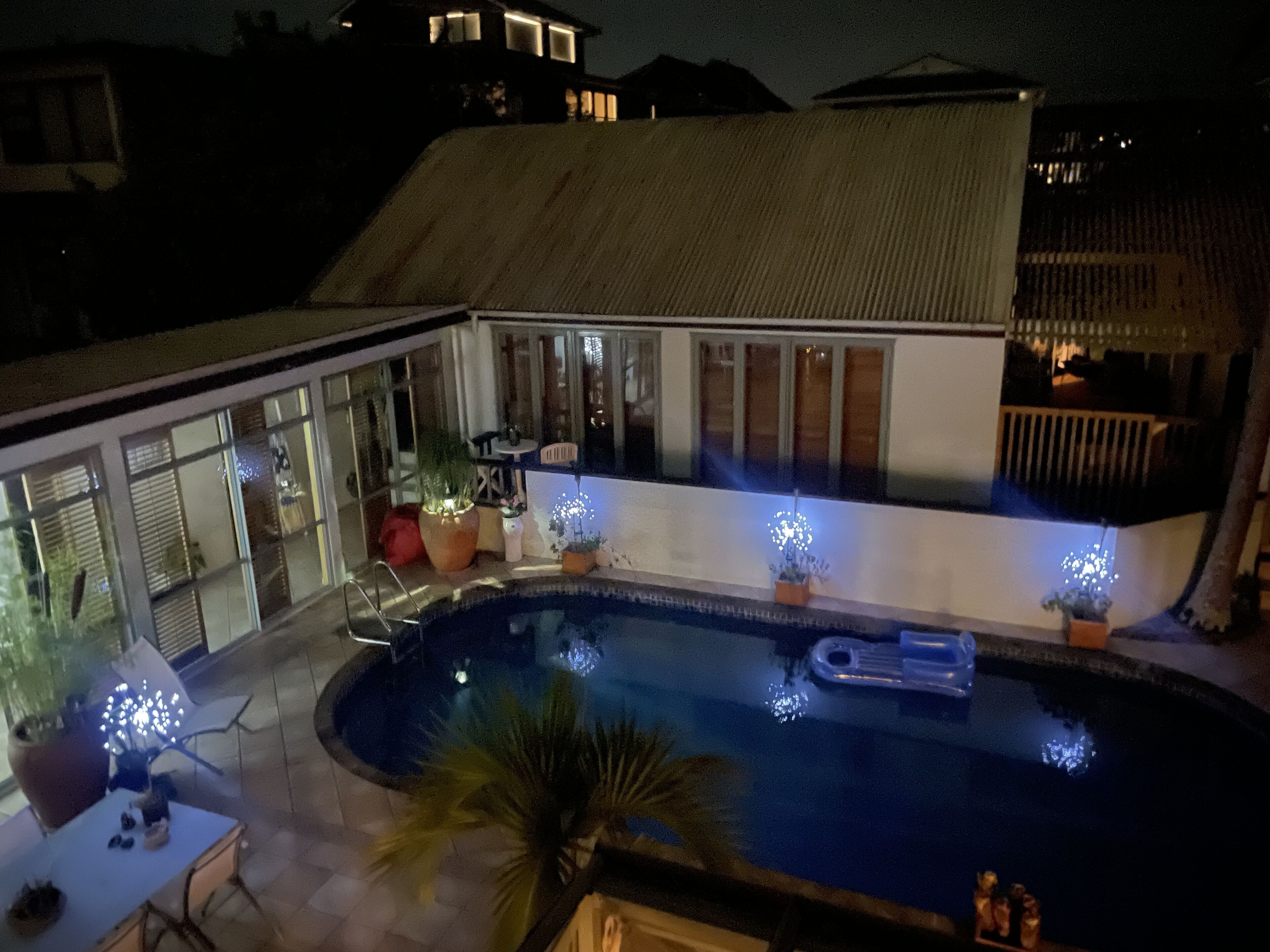 A swimming pool with a sunken seating area, surrounded by potted plants and a patio table.