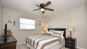 A bedroom with a bed, bedside tables, a ceiling fan, a window, and wall decorations.