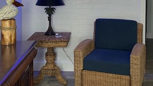 Ein Zimmer mit Wandbild eines blauen Fisches, einem Korbstuhl, einer Lampe und einem Holztisch mit einer Vogel-Figur.