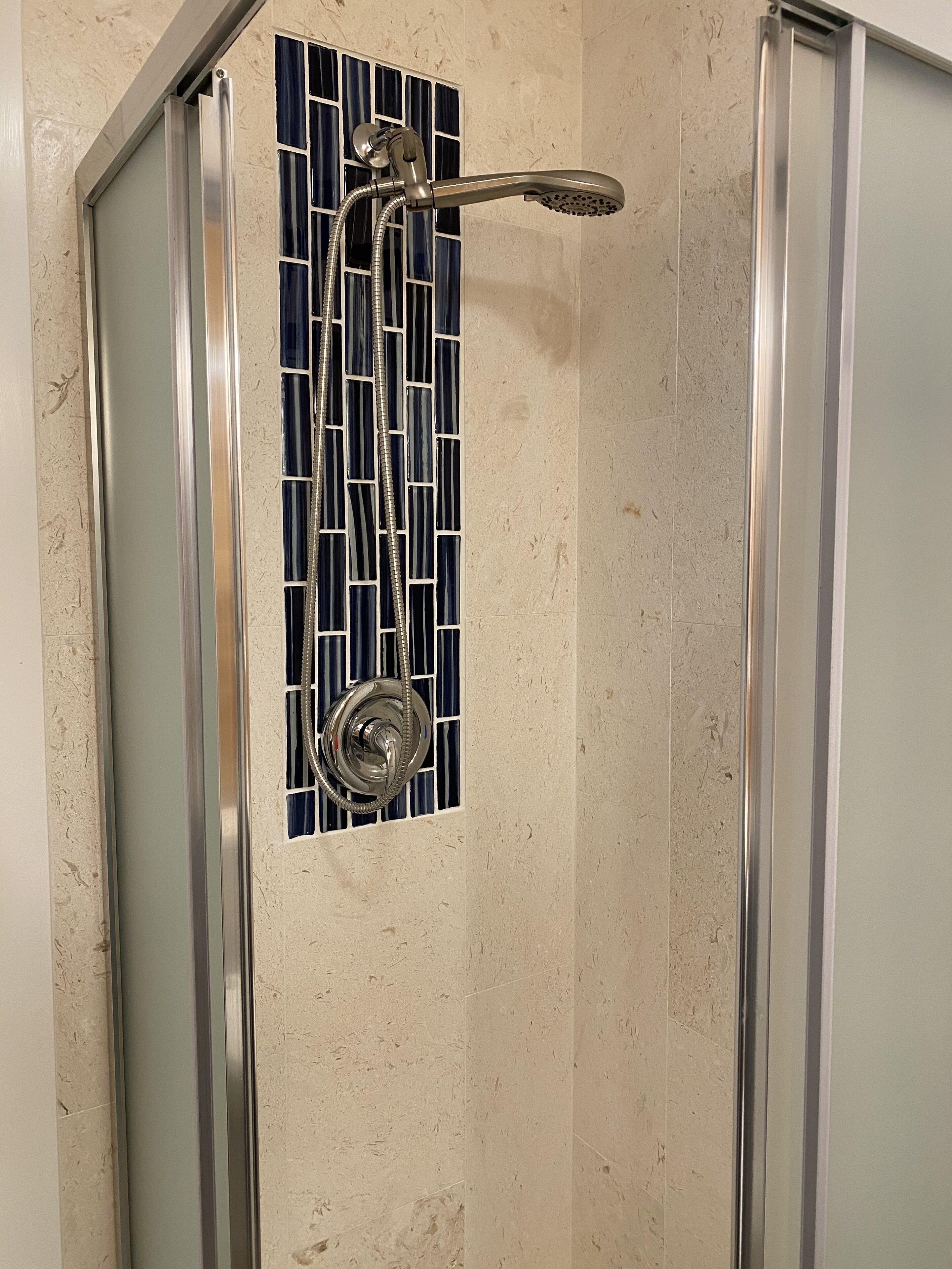 A shower with a chrome showerhead and a glass panel with a blue and white pattern.