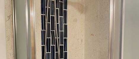 A shower with a chrome showerhead and a glass panel with a blue and white pattern.