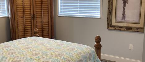 A bedroom with a bed, a ceiling fan, a wardrobe, a window with blinds, and a framed picture on the wall.