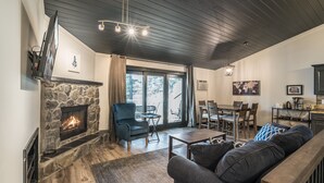 Ett mysigt vardagsrum med en öppen spis i sten, en bekväm soffa och en matplats med ett bord och stolar.