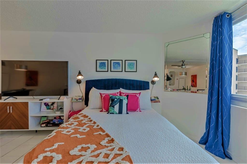 A bedroom with a bed, bedside lamps, a TV, a wardrobe, and a mirror.