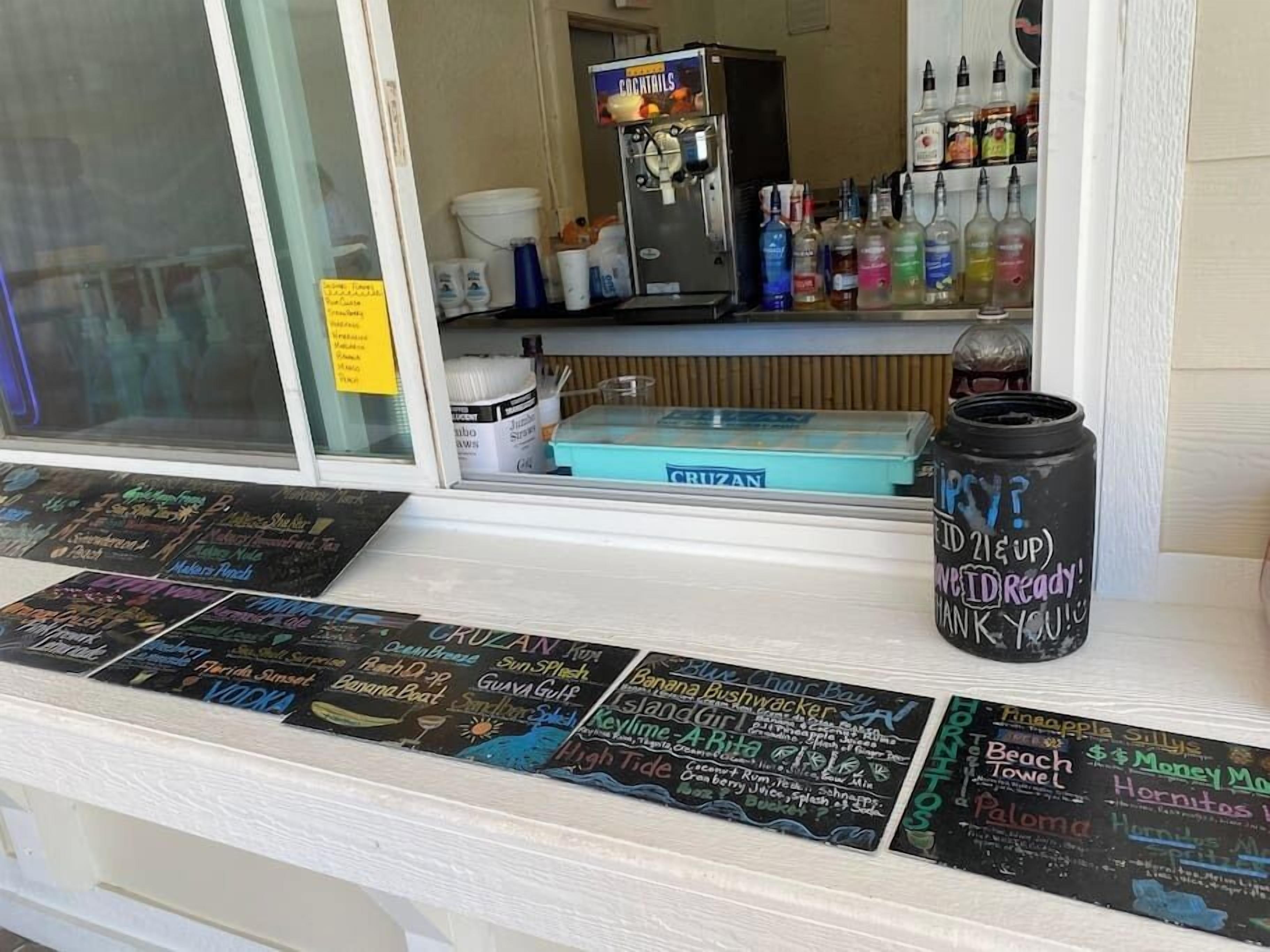 Un espace bar avec un tableau affichant le menu, un distributeur de boissons et un assortiment de bouteilles.