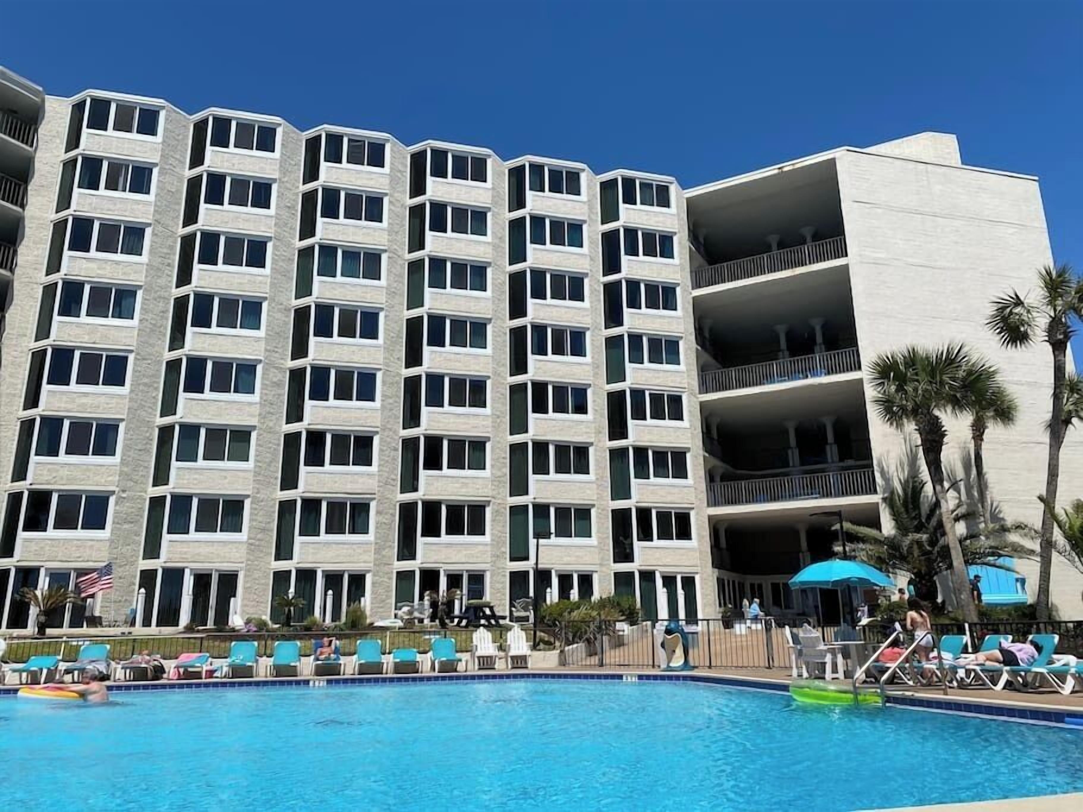 A multi-story hotel with a swimming pool, outdoor seating, and palm trees.