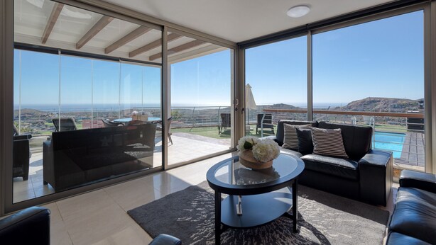 A spacious balcony with a black leather sofa, a glass table with a decorative bowl, and a view of a swimming pool and distant landscape. - Spectacular villa with private pool, sea views, barbecue and relaxing environment (San Bartolomé de Tirajana)