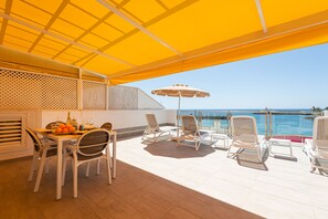 A sunlit outdoor patio with a dining table, chairs, and a large umbrella.