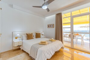 A hotel room with a bed, a nightstand, a ceiling fan, a window with curtains, and a view of the outside.