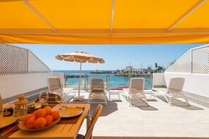 A terrace with a table set for dining, lounge chairs, and a view of the sea.