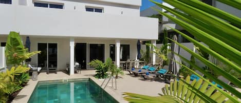 Un edificio moderno con piscina, mobiliario exterior y plantas tropicales.