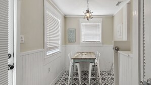 A narrow hallway with white paneled walls, a wooden table with chairs, and a decorative ceiling light. - {Laguna Shores} 1 Block 2 Beach + Pool-Dogs OK (Panama City Beach)