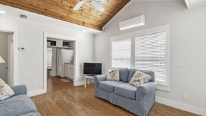 A modern living room with a grey sofa, a flat-screen TV, and a wooden ceiling. - {Laguna Shores} 1 Block 2 Beach + Pool-Dogs OK (Panama City Beach)