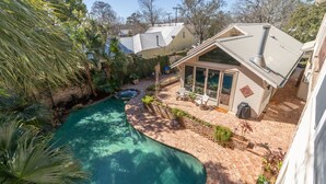 A backyard with a swimming pool, a patio with chairs, and a small building with a sloped roof. - Coquille Cottage located in Historic Madisonville (Madisonville)