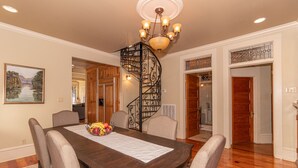 A dining area with a wooden table, chairs, a chandelier, and a spiral staircase. - Coquille Cottage located in Historic Madisonville (Madisonville)