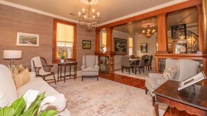 A spacious living room with a large wooden-framed mirror, a chandelier, and a dining area with a table and chairs. - Coquille Cottage located in Historic Madisonville (Madisonville)
