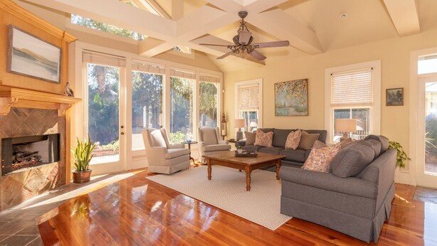 A spacious living room with hardwood floors, a fireplace, a ceiling fan, and large windows allowing natural light. - Coquille Cottage located in Historic Madisonville (Madisonville)