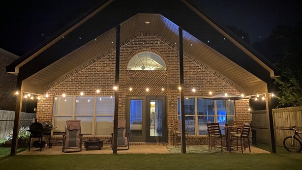 Una casa de ladrillo con un porche cubierto, luces colgantes y mobiliario de exterior.