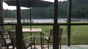 Un espacio al aire libre techado con una mesa y sillas, con vistas a un lago y una zona boscosa.
