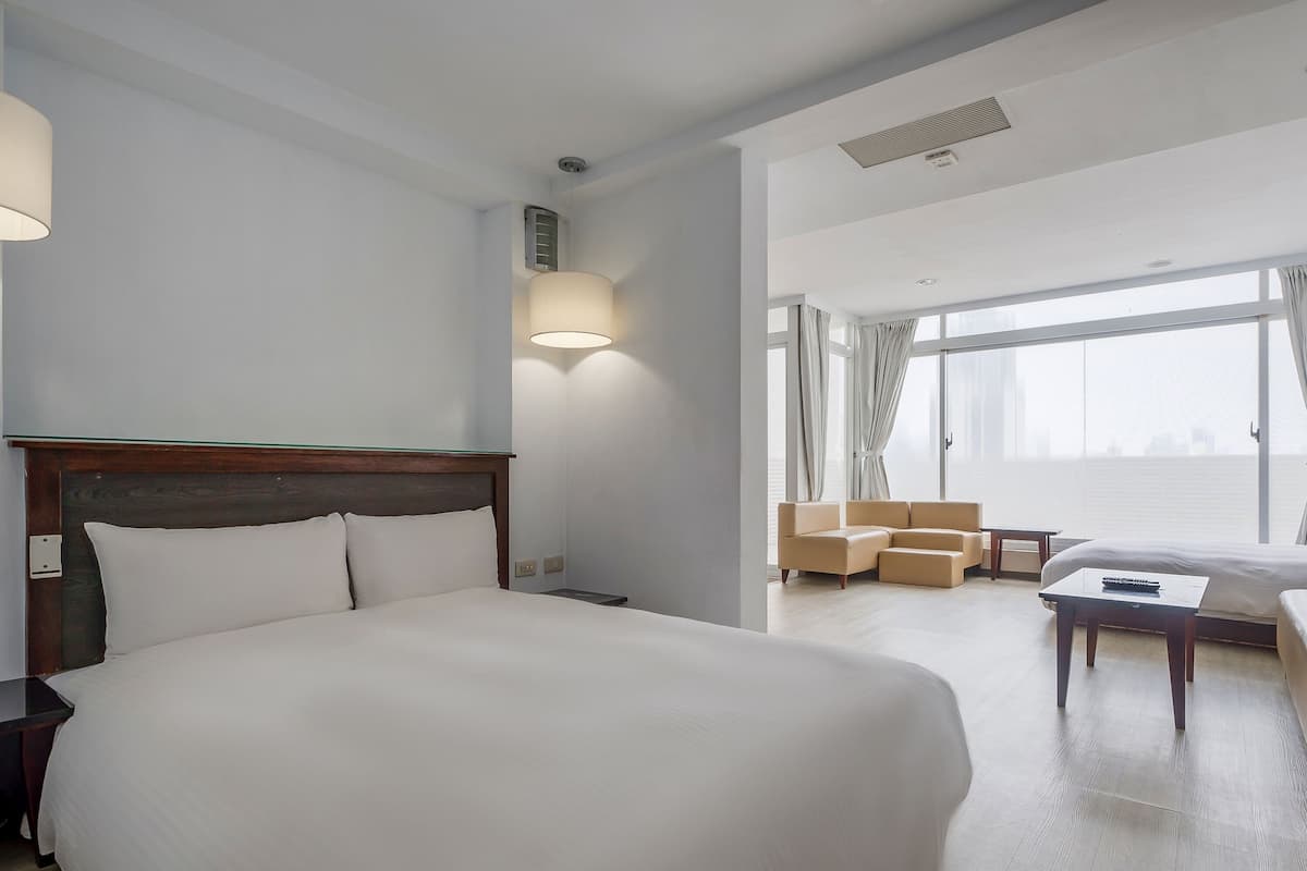 Habitación de hotel con una cama grande, una mesita de noche, una lámpara, un sofá y vistas a la ciudad.