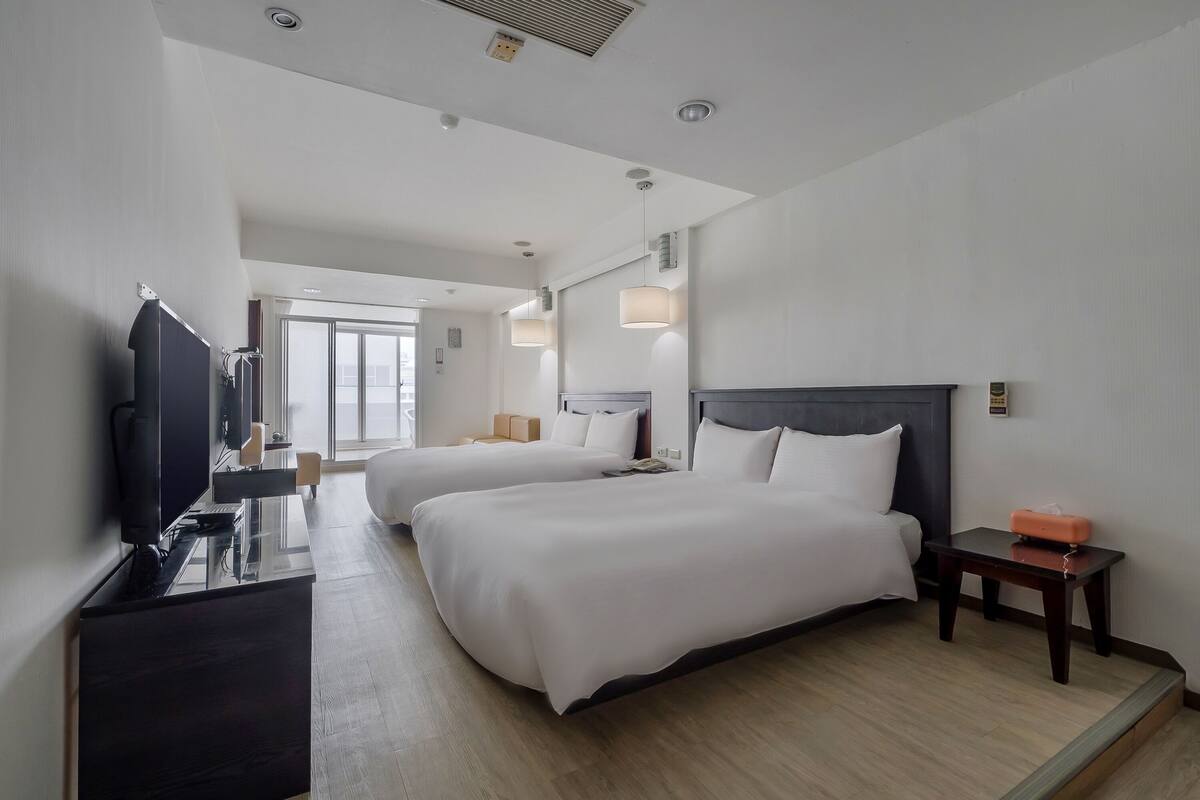 Habitación de hotel con dos camas, televisión, escritorio y una mesita.